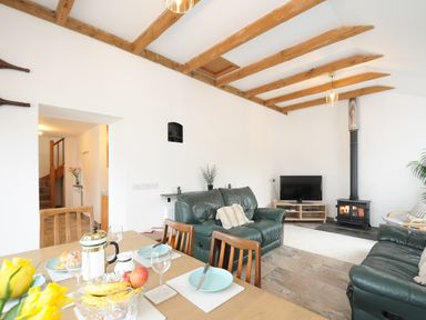 A living room with green leather sofas a dining table with plates and fruit and a wood burning stove at The Dairy Barn in Camelford