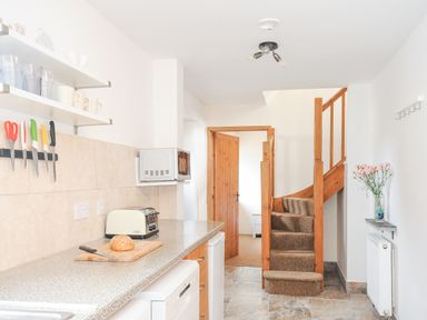 A kitchen with knives on a magnetic strip a toaster a microwave and stairs at The Dairy Barn in Camelford