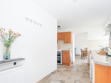 A kitchen with wooden cabinets a countertop a stove and a dining table in the background at The Dairy Barn in Camelford