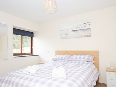 A bedroom with a double bed with checkered bedding two bedside tables and a window at The Dairy Barn in Camelford
