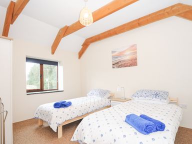 A bedroom with two single beds a window and wooden ceiling beams at The Dairy Barn in Camelford