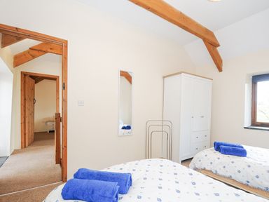 A bedroom with two single beds with blue towels a white wardrobe and a window at The Dairy Barn in Camelford