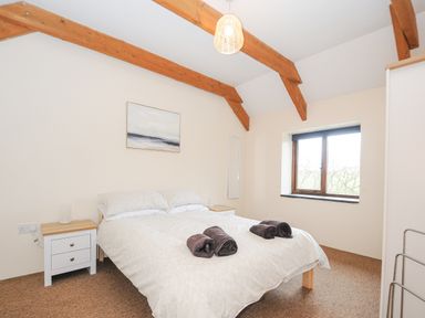 A bedroom with a bed two rolled towels two bedside tables with lamps a window and exposed wooden ceiling beams at The Dairy Barn in Camelford