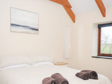 A bedroom with a bed with white bedding and towels on it a bedside table a window and a painting on the wall at The Dairy Barn in Camelford