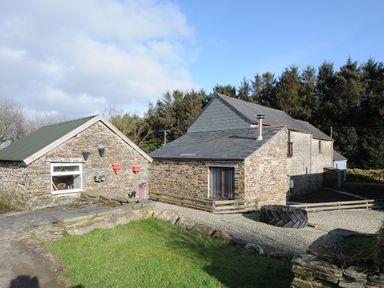 An outdoor view of stone buildings with slate roofs gravel driveway and grass area at The Dairy Barn in Camelford