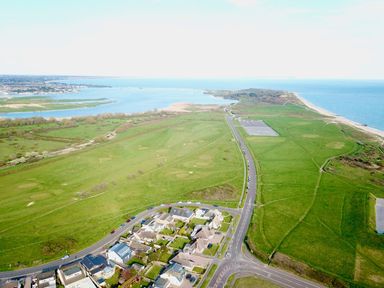 Aerial view of a coastal area with houses roads green fields a golf course and a beach at Bayview Cottage in Southbourne