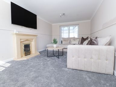 A living room with a beige fireplace a wall-mounted TV a light-colored sofa a round coffee table with a plant and glass doors at 9 Beckett Close in Colwyn Bay