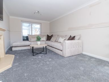 A living room with a beige sectional sofa a round wooden coffee table with a plant on it and a beige fireplace at 9 Beckett Close in Colwyn Bay