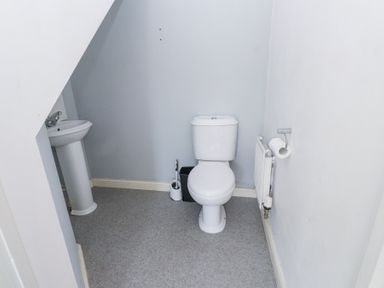 A small bathroom with a toilet a sink a toilet brush a trash bin a radiator and a toilet paper holder at 9 Beckett Close in Colwyn Bay