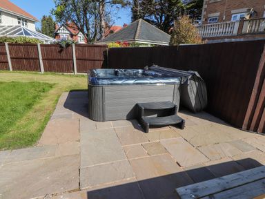 A backyard with a hot tub on a stone patio next to a grass lawn and wooden fence at 9 Beckett Close Colwyn Bay