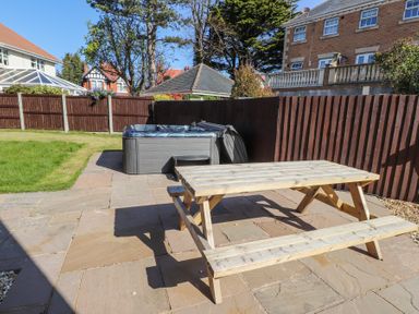 A backyard patio with a wooden picnic table and a hot tub surrounded by a wooden fence at 9 Beckett Close in Colwyn Bay