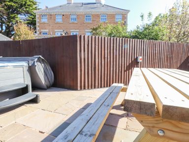 An outdoor patio area with stone paving a wooden picnic table a covered hot tub and a wooden fence at 9 Beckett Close in Colwyn Bay