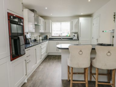 A kitchen with appliances and bar stools at 9 Beckett Close in Colwyn Bay