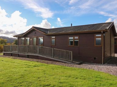 A wooden single-story house with a wheelchair ramp on a grassy lawn at Crathie Lodge in Banavie near Caol
