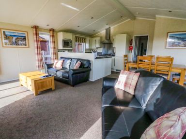 An open living room and kitchen area with black leather sofas a wooden coffee table dining table and kitchen appliances at Crathie Lodge Banavie near Caol