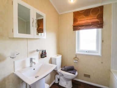 A bathroom with a sink toilet mirror cabinet and window with brown blind at Crathie Lodge in Banavie near Caol