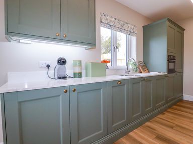 A kitchen with green cabinets a coffee machine containers a sink and a window at Little Hillside in Redruth