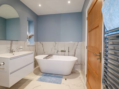 A bathroom with a freestanding bathtub a vanity with sink a mirror and a wooden door at Little Hillside in Redruth