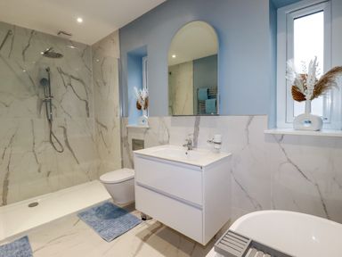 A bathroom with a walk in shower toilet sink with mirror and a window with a vase at Little Hillside in Redruth