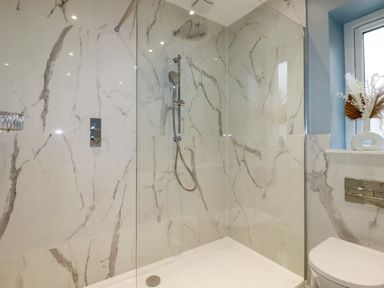 A bathroom with a walk-in shower with marble wall tiles a showerhead a window and a toilet at Little Hillside in Redruth