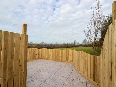 A fenced outdoor patio area with tiled flooring and a grassy field beyond at Little Hillside in Redruth