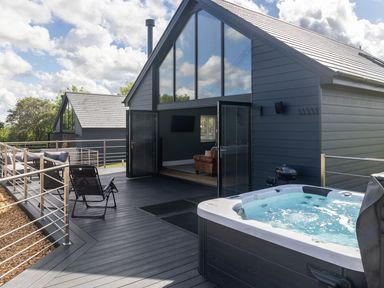 An outdoor deck with a hot tub lounge chairs and open doors leading to a living room at Hares Hill in Thornton Le Dale