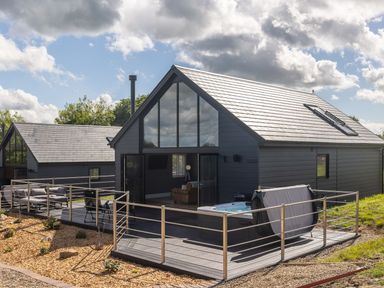 Modern two house buildings with large glass windows a deck with seating and a hot tub at Hares Hill in Thornton-Le-Dale