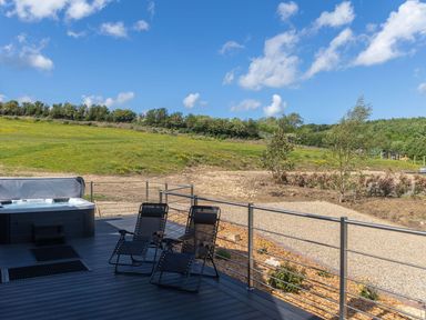 A deck with two black lounge chairs and a hot tub overlooking a grassy field and trees at Hares Hill in Thornton-Le-Dale