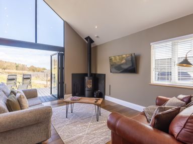 A living room with a grey sofa a brown leather sofa a wood stove and a TV on the wall at Hares Hill in Thornton-Le-Dale
