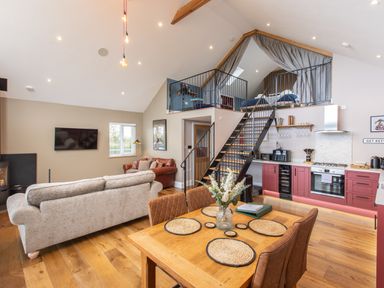 An open plan living room and kitchen with a wooden dining table and chairs a staircase leading to a loft bedroom at Hares Hill in Thornton Le Dale