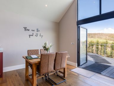A dining area with four chairs around a wooden table and a glass door opening to a deck at Hare's Hill in Thornton-Le-Dale