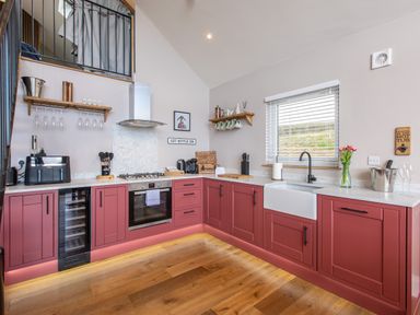A kitchen with red cabinets a white farmhouse sink hanging mugs near a window and wooden floor at Hares Hill in Thornton-Le-Dale