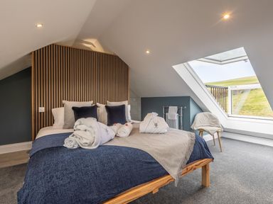 A bedroom with a wooden bed frame and pillows near a large slanted window showing an outdoor view at Hares Hill in Thornton-Le-Dale