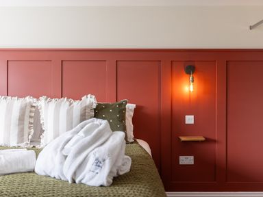 A bed with striped and patterned pillows green blanket and folded white robes next to a red paneled wall with a wall light and switch at Hares Hill in Thornton-Le-Dale