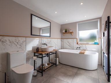 A bathroom with a toilet a freestanding bathtub a sink on wooden countertop a mirror and a window at Hares Hill in Thornton-Le-Dale
