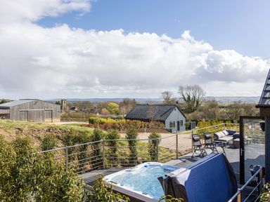 An outdoor deck with a hot tub chairs and a sofa overlooking countryside and buildings at Hares Hill in Thornton-Le-Dale