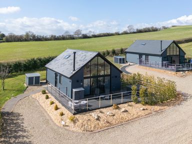 Two modern grey houses with large front windows and decks surrounded by gravel and landscaping in a rural area at Hares Hill in Thornton-Le-Dale