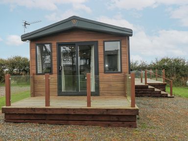 A small wooden cabin with glass sliding doors and a deck with glass railing at Caldey Retreat in Hasguard Cross near Broad Haven