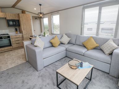 A living room with a grey sectional sofa and a wooden coffee table next to a kitchen with wooden cabinets at Caldey Retreat Hasguard Cross near Broad Haven