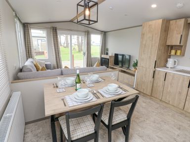 A dining area with set table and chairs next to a living room with sofa and television at Caldey Retreat in Hasguard Cross near Broad Haven