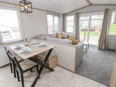 A dining table with chairs and a bench next to a sofa in a living area with large windows and sliding doors at Caldey Retreat Hasguard Cross near Broad Haven