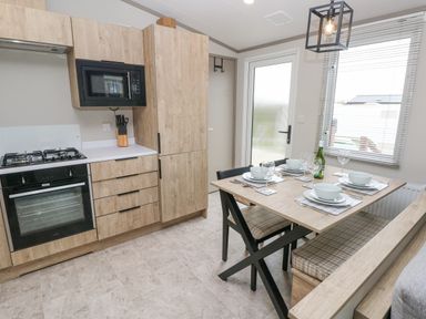 A kitchen and dining area with wooden cabinets and a set dining table at Caldey Retreat in Hasguard Cross near Broad Haven