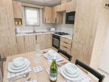 A kitchen with wooden cabinets a dining table set with plates bowls glasses and utensils at Caldey Retreat in Hasguard Cross near Broad Haven