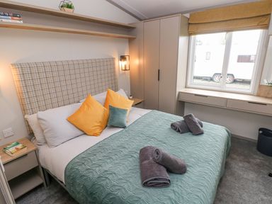 A bedroom with a double bed featuring yellow and green pillows a teal bedspread and rolled towels beside a window at Caldey Retreat Hasguard Cross near Broad Haven