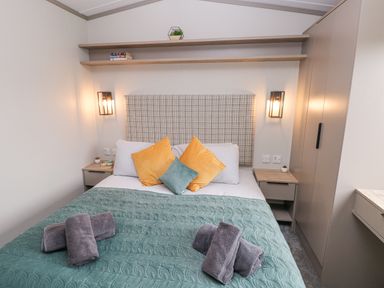 A bedroom with a bed with pillows and folded towels on a quilt and a wardrobe on the side at Caldey Retreat in Hasguard Cross near Broad Haven