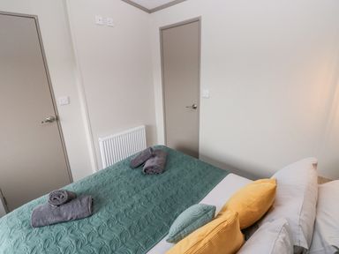 A bedroom with a bed having green quilt and yellow and green pillows with two closed beige doors at Caldey Retreat in Hasguard Cross near Broad Haven
