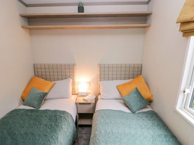 A bedroom with two single beds side by side with patterned headboards and a nightstand with a lamp between at Caldey Retreat in Hasguard Cross near Broad Haven