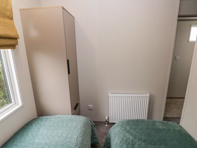 A bedroom with two single beds with green covers a wardrobe radiator and a window at Caldey Retreat Hasguard Cross near Broad Haven