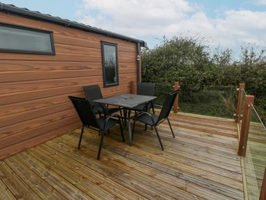 A wooden deck with a table and four chairs attached to a building with wood siding at Caldey Retreat Hasguard Cross near Broad Haven