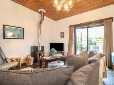 A living room with a fireplace a TV wooden coffee table gray sofa and sliding glass door at Owl Cottage in Ashen Cross Pelynt